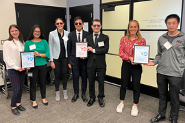 3 teams, with 7 people total, pose for a photo inside a meeting room, and the teams hold 3 framed MADMEC awards announcing their placement. The team in center wears sunglasses and suits.