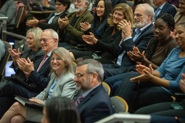 Rows of people sit and applaud in a filled auditorium. Sally Kornbluth and L. Rafael Reif are among those in the front row.