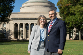 Sally Kornbluth and Daniel Lew, standing close together, pose for a photo on Killian Court, with MIT’s Great Dome in the background.