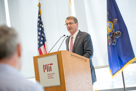 Ashton Carter in a suit speaking behind a wooden podium with sun filled windows behind him