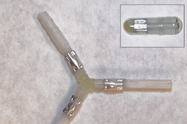 Photo shows a Y-shaped device made of beige elastomer and shiny aluminum. Inset photo on top right shows a pill-shaped device with similar coloring.