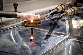 Photo shows 3D-printed superalloy glowing white with heat. Two unique tools, made of metal and white material, are used to handle the glowing superalloy.