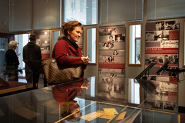 A woman stands at a display case at the exhibit, watching an iPad. Background includes posters with photos and text that says “MIT in South Asia.”