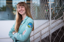 Skylar Larsen smiles indoors, and her jacket has a patch that says “MIT Wallace Astrophysical Observatory.” 