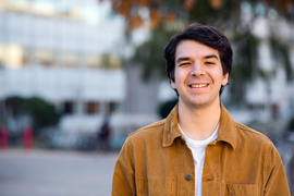 Jack Cook smiles, standing in front of an out-of-focus white building