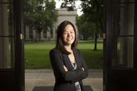 Evelyn Wang stands, smiling with arms folded, in a doorway looking out to the green lawn and trees of MIT's Killian Court
