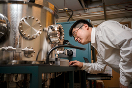 Luqiao Liu looks inside the porthole of a large cylindrical device in the lab.