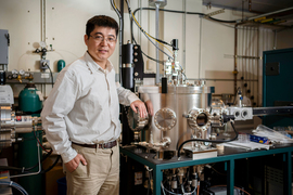 Liu stands with his arm on a large metallic device inside the lab.
