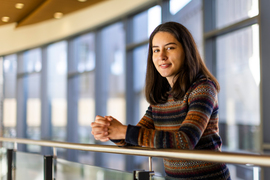 Valeria Robayo leans against a railing with MIT Sloan windows in background.