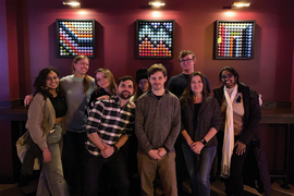 9 people, including Laurie Boyer, smile for a group photo, with 3 pixelated-style artworks in background.