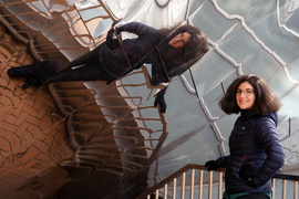 Tamara Broderick stands outside the Stata Center and its reflective façade fills the background. Her reflection spreads dramatically across the photo.