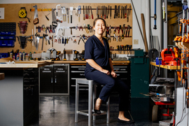 Mazereuw sits on a stool in her MIT workshop with a wall of saws, clamps, and other tools in the background.