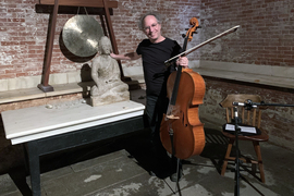 Tod Machover holds onto cello while posing next to a statue and gong.