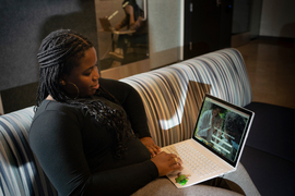 Oladipo sits on a couch inside the IHQ building with her laptop. On the screen is the Birth By Us website, with the words, “We would love to share your story.”