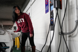 A person wearing an MIT shirt charges their electric vehicle in an indoor parking lot.