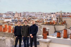 Raber, Levi, and Cousin stand together on a roof, and in the background are the roofs of Paris, with many orange chimneys.
