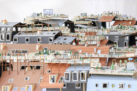 A stunning architectural miniature seems to be made of paper and wood, and shows gardens on a variety of roofs in a busy, modern city. There are several textures and roofing styles, and the gardens have white railings, umbrellas, chairs, and even a movie screen in the background.