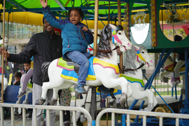 A young child waves while riding a horse on a carousel.