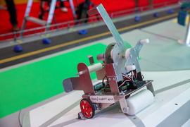 A close-up shows the robot Gambit, which has 2 red wheels and 1 roller wheel in the front, as it climbs a ramp. Gears and wires are visible.