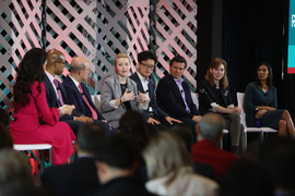 A moderator and seven MIT faculty members sit on stage. Professor Anne White, in the center, is speaking while the others look on.