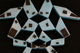 The back of the kirigami blue heart in mid-transformation into a triangle. Black pieces are attached to the back.