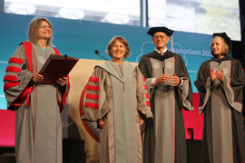 Sally Kornbluth, Diane Greene, L. Rafael Reif, and Susan Hockfield stand on stage wearing academic regalia and smiling.