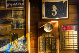 The wall features an old blue flag with a seahorse, newspaper clippings, and awards.