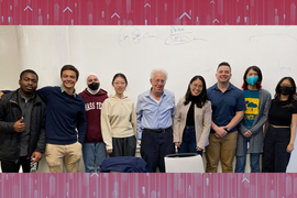 9 people take a group photo in front of a white board, and some wear masks and MIT-branded clothing. Pozen smiles in the center.