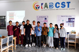 10 people pose for a group photo inside a classroom, holding medal medallions, with a painted logo on the wall saying “Fab Lab CST, College of Science and Technology, Bhutan.”