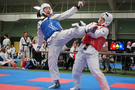 In the middle of a Taekwondo tournament, an athlete in blue, on left, does a dramatic high kick at a competitor in red
