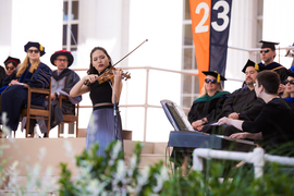 Shelley Choi playing the violin on stage while MIT faculty members watch behind her.