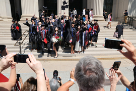 On the steps of MIT’s main entrance, a group of graduates throw their hats in the air and pose for many spectators taking photos.