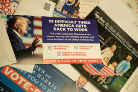 Three postcard-sized printed ads with political slogans are on a flat surface: one with Donald Trump, one with President Joe Biden, and another with a family holding the US flag.