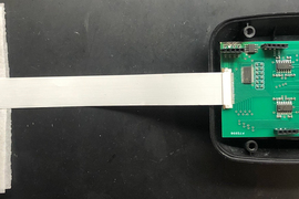 A photo shows a test setup. The sensor is on left, and it is connected to a small circuit board. A long strip connects that to a larger cellphone-sized circuit board incased in plastic.