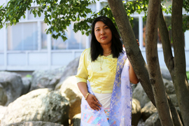 Ukheng is outside with her hand resting on a tree, with the rocky Stata Center Swale and the Whitaker Building in background.