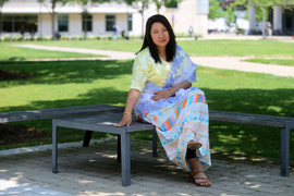 Ukheng sits on a bench with legs crossed, with Hockfield Court in background.