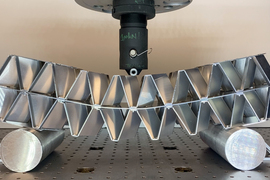 A long modular aluminum object is put under stress as a machine pushes down on the middle of it.