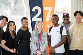 Melissa Nobles, Sally Kornbluth, and MIT students and five other community members pose in front of a flag that says “27.”