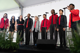 Kornbluth, center, sings with 8 members of The Chorallaries, all wearing red and black outfits.