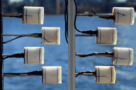 Eight piezoelectric transducers look like toilet paper rolls and are attached to poles, near water.