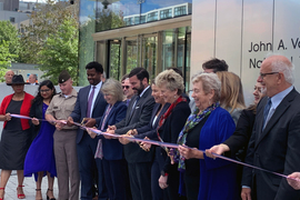 A line of people including President Sally Kornbluth, Governor Maura Healey, and about 13 others cutting a ribbon.