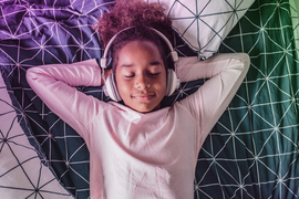 A kid relaxes while listening to headphones on their bed.