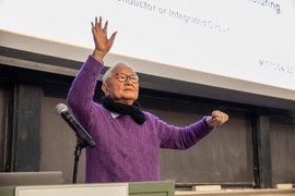 Morris Chang gestures with his hands while at the podium, in front of a screen.