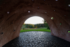 A view of green countryside seen through the arched entrance of the brick sculpture