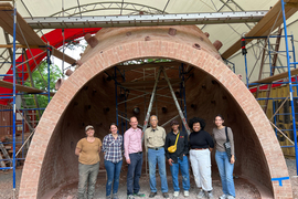 7 people stand inside the partially built structure, with ladders and equipment around the structure. From left to right: Lara Davis, Rebecca Buntrock, John Ochsendorf, Martin Puryear, Nebyu Haile, Nia Rich, and Domonique Valenzuela.