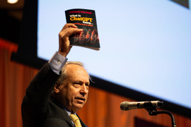 Rodney Brooks holding up a book while speaking
