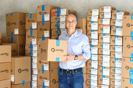 Jorge Schippers holds a cardboard box and smiles while surrounded by more boxes, all with the Pacifiko logo on them.