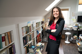 Wiebke Denecke stands with arms crossed, and the office is filled with stacks of books.