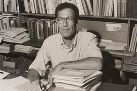 Black-and-white photo of Robert Solow at his desk with a filled bookcase behind him