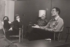 Black-and-white photo of Robert Solow sitting in a small room, speaking with Paul Gray and two others